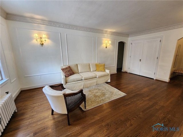 living room with dark wood-style floors, baseboards, radiator heating unit, arched walkways, and a decorative wall