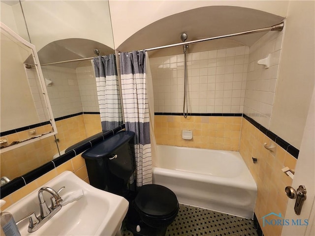 full bathroom featuring toilet, tile walls, shower / tub combo with curtain, and a sink