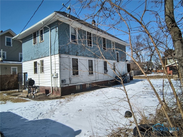 snow covered property with fence, a chimney, and a patio area