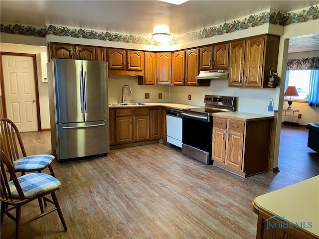 kitchen featuring wood finished floors, a sink, stainless steel appliances, light countertops, and under cabinet range hood