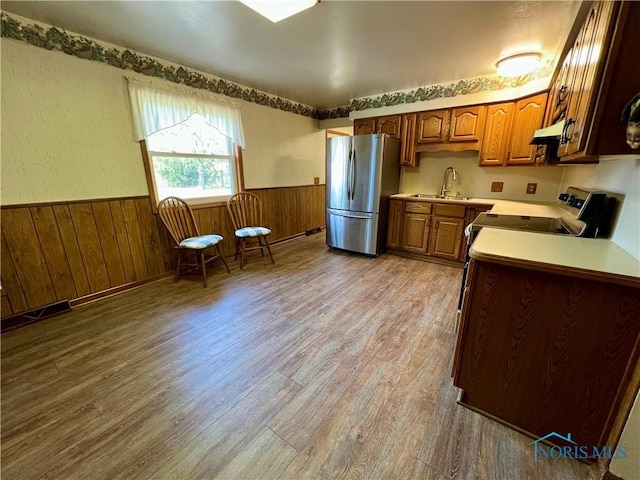 kitchen with a sink, a wainscoted wall, under cabinet range hood, and stainless steel appliances