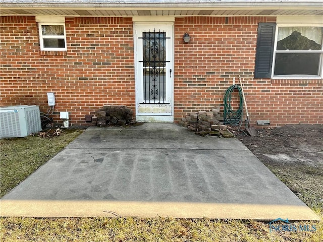 view of exterior entry featuring central air condition unit, brick siding, and crawl space