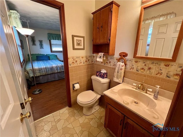 bathroom featuring a wainscoted wall, toilet, ensuite bathroom, tile walls, and vanity