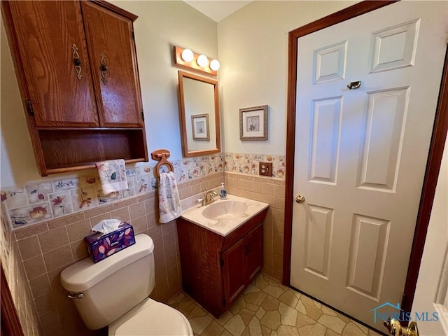 half bath featuring a wainscoted wall, toilet, tile walls, and vanity