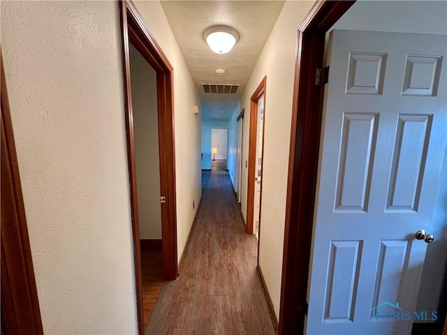 corridor featuring a textured wall, visible vents, baseboards, and wood finished floors