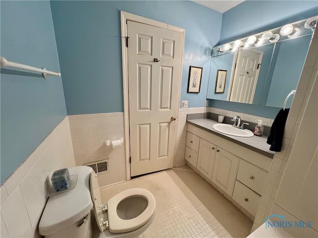 bathroom featuring visible vents, tile walls, toilet, wainscoting, and vanity