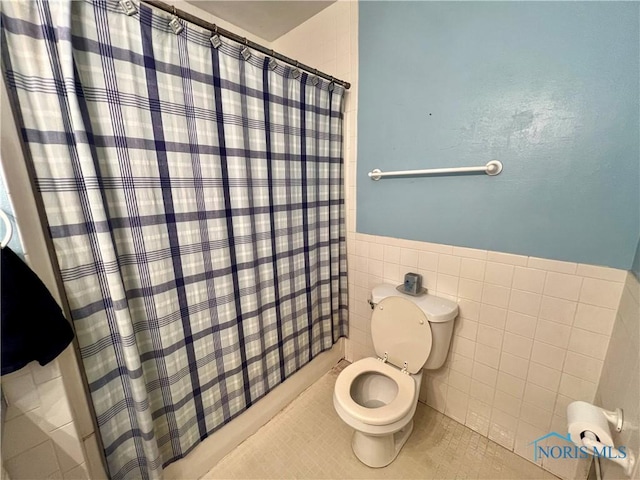 bathroom featuring tile patterned flooring, a wainscoted wall, toilet, a shower with shower curtain, and tile walls