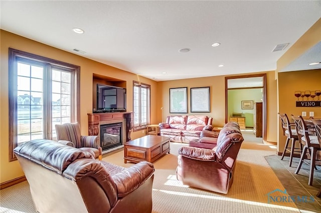 living area with a glass covered fireplace, recessed lighting, and visible vents