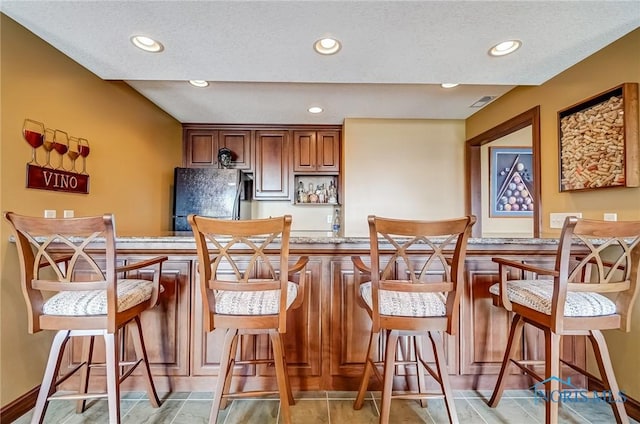 kitchen with visible vents, light stone countertops, a breakfast bar area, recessed lighting, and freestanding refrigerator