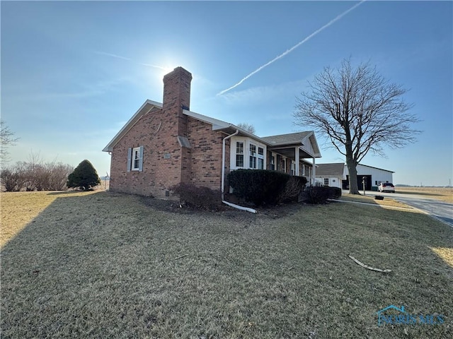 view of side of property featuring brick siding, a chimney, and a yard