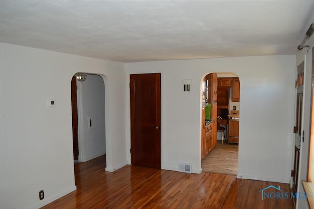 spare room with arched walkways, visible vents, baseboards, and wood finished floors