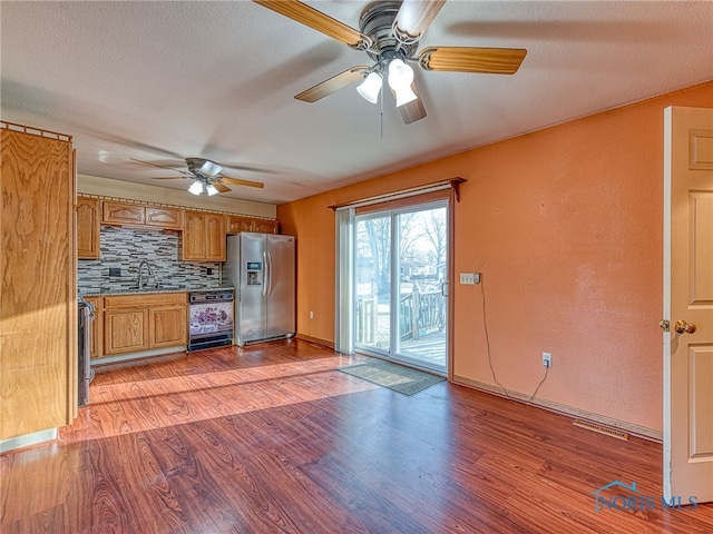 kitchen with light wood finished floors, stainless steel fridge with ice dispenser, decorative backsplash, brown cabinetry, and a sink