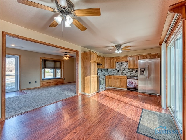 kitchen with backsplash, under cabinet range hood, open floor plan, appliances with stainless steel finishes, and light wood-style floors