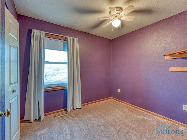 carpeted spare room featuring visible vents, baseboards, a textured wall, a textured ceiling, and a ceiling fan