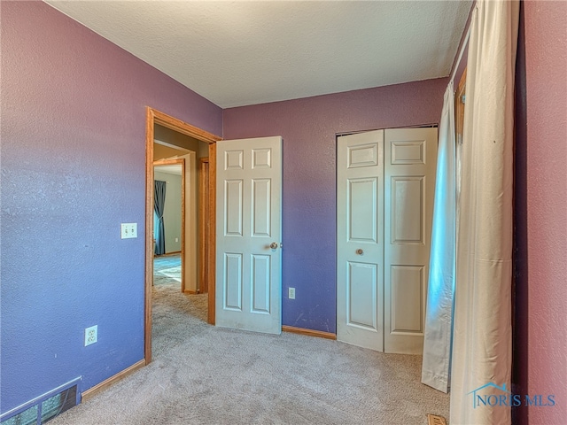 unfurnished bedroom featuring visible vents, carpet flooring, a textured wall, a closet, and a textured ceiling