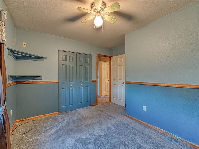 unfurnished bedroom featuring a ceiling fan, a closet, a textured ceiling, carpet flooring, and a textured wall