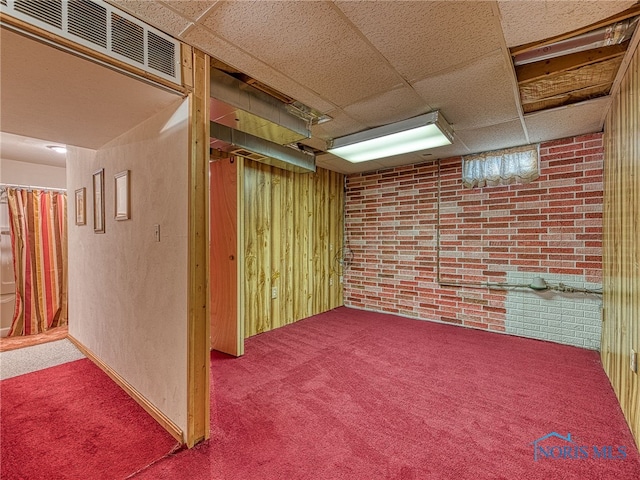 finished below grade area featuring brick wall, carpet flooring, visible vents, and a drop ceiling