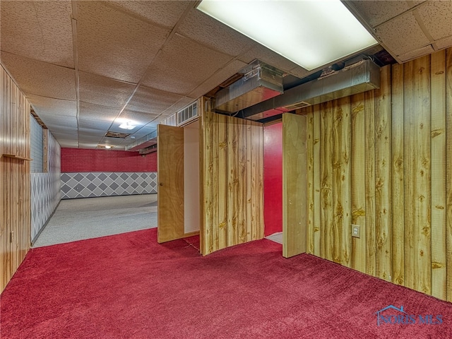 finished basement featuring wooden walls, a drop ceiling, visible vents, and carpet floors