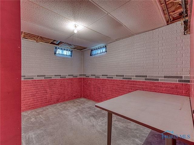 below grade area featuring a paneled ceiling, brick wall, and carpet flooring