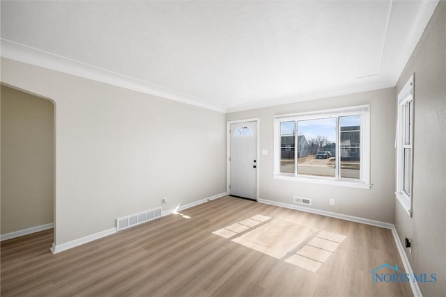 empty room featuring arched walkways, wood finished floors, visible vents, and baseboards