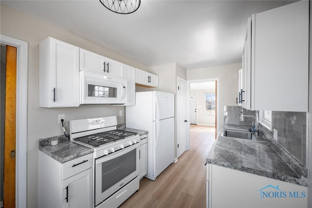 kitchen featuring white appliances, a sink, light wood-style floors, white cabinetry, and dark countertops