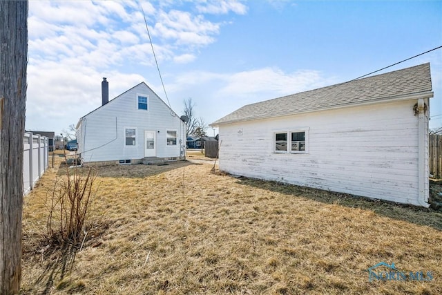 rear view of property featuring a shingled roof, fence, a lawn, and a chimney