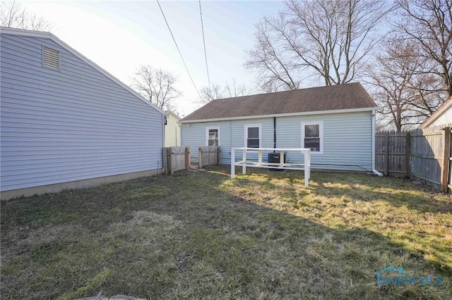 rear view of house featuring fence, a lawn, and roof with shingles