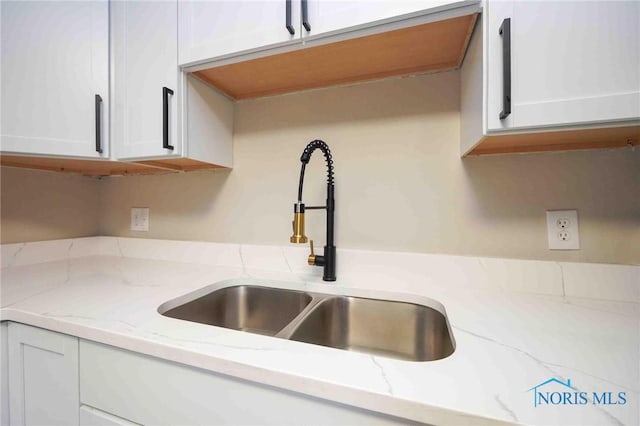 kitchen with a sink, light stone countertops, and white cabinetry