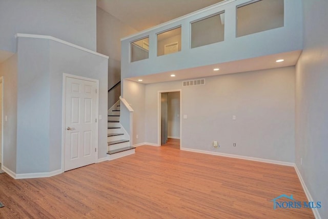 interior space with baseboards, visible vents, a high ceiling, light wood-style flooring, and stairs