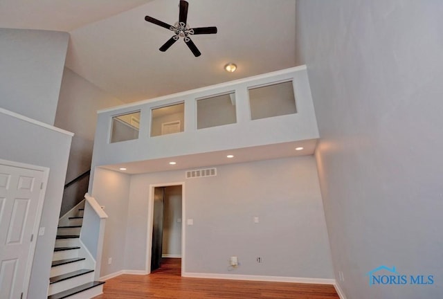 unfurnished living room featuring a ceiling fan, wood finished floors, visible vents, high vaulted ceiling, and stairs