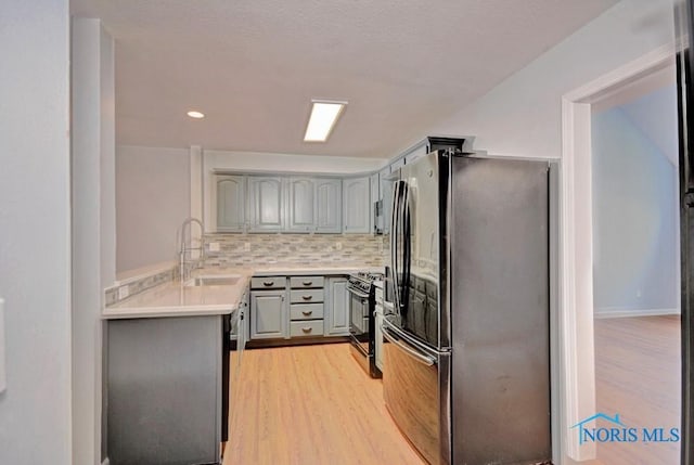 kitchen featuring gray cabinets, freestanding refrigerator, a sink, black range with gas stovetop, and tasteful backsplash