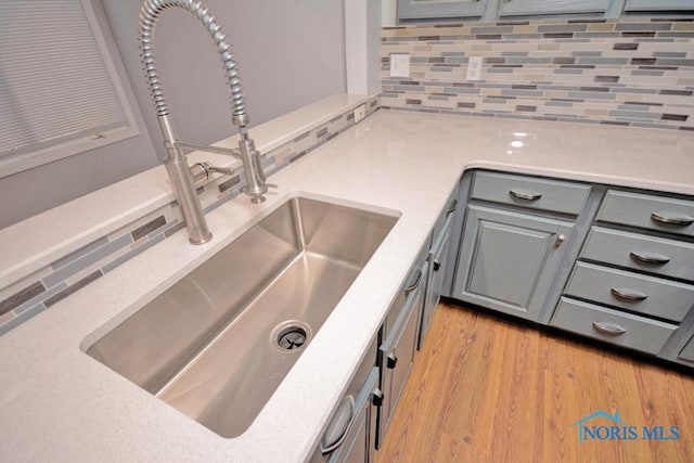 interior details featuring light wood-type flooring, gray cabinetry, a sink, tasteful backsplash, and light countertops