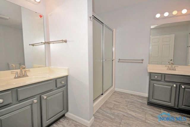 full bath with a stall shower, two vanities, baseboards, and a sink