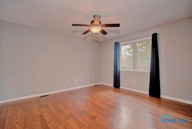 spare room with visible vents, a ceiling fan, baseboards, and wood finished floors