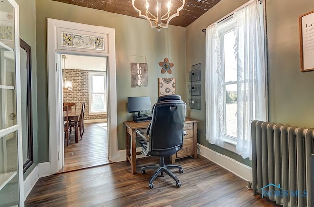 office featuring radiator, brick wall, baseboards, wood finished floors, and a notable chandelier