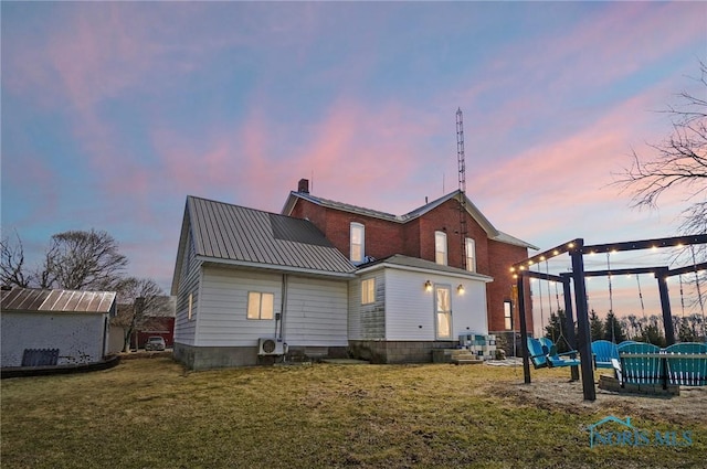 back of house at dusk with metal roof, an outbuilding, a lawn, and a chimney