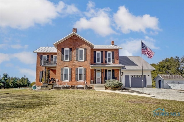 colonial inspired home with a balcony, a standing seam roof, a chimney, concrete driveway, and brick siding