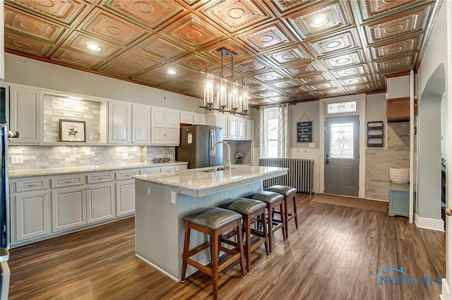 kitchen with dark wood-type flooring, an ornate ceiling, freestanding refrigerator, radiator, and white cabinets