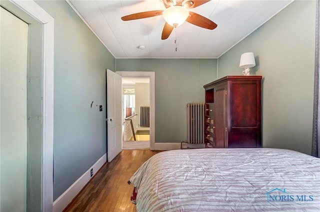 bedroom with a ceiling fan, radiator, wood finished floors, and baseboards