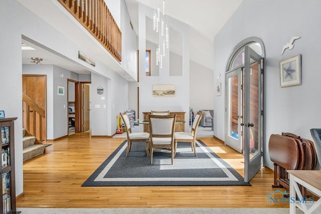 dining space featuring wood finished floors, baseboards, stairs, french doors, and a towering ceiling