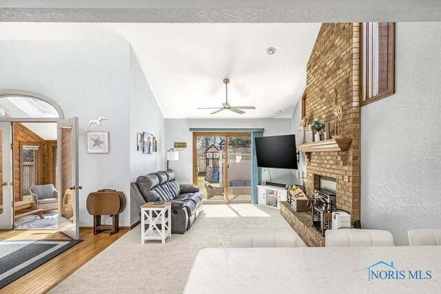 living room with baseboards, vaulted ceiling, a fireplace, wood finished floors, and a ceiling fan