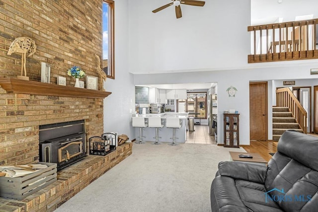 living area featuring stairs, a high ceiling, a ceiling fan, and light carpet