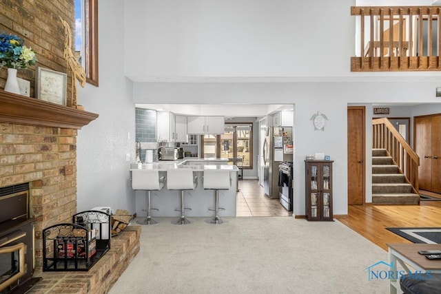 living room featuring stairs, a brick fireplace, a towering ceiling, and light carpet