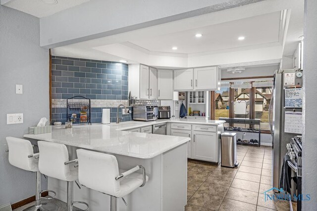 kitchen with stainless steel range with gas cooktop, a peninsula, a sink, decorative backsplash, and white cabinetry