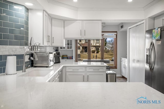 kitchen featuring crown molding, light stone counters, decorative backsplash, stainless steel refrigerator with ice dispenser, and a sink