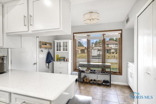 kitchen with light tile patterned floors, light stone countertops, baseboards, a peninsula, and white cabinets