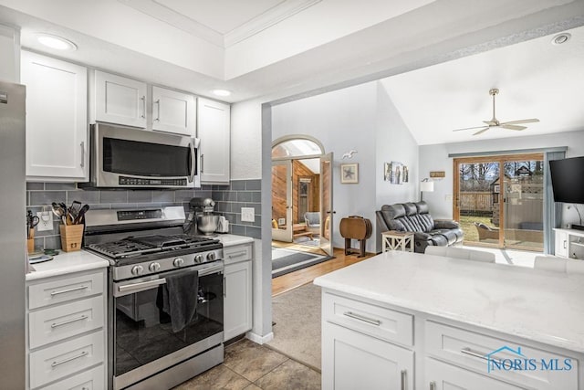 kitchen featuring tasteful backsplash, crown molding, open floor plan, appliances with stainless steel finishes, and white cabinets