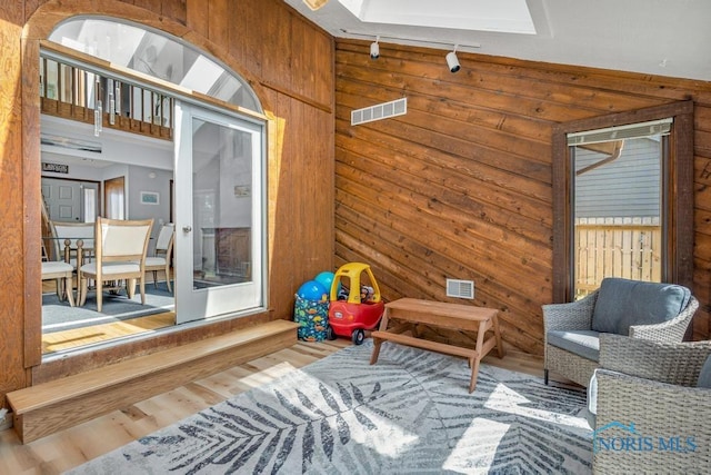 sitting room with track lighting, wooden walls, wood finished floors, and visible vents