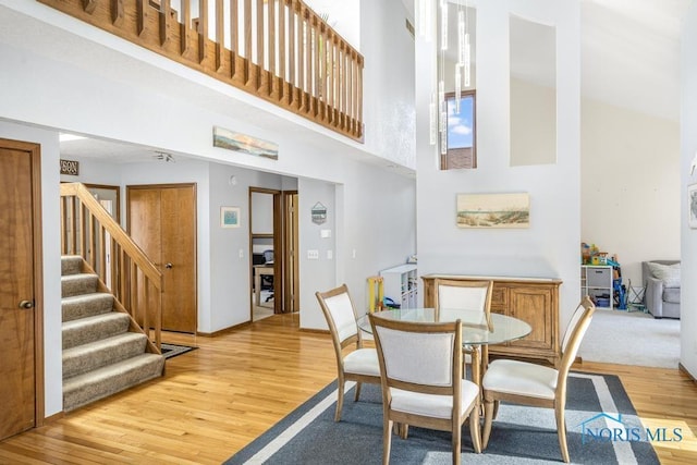 dining area with stairs, light wood-type flooring, and a high ceiling