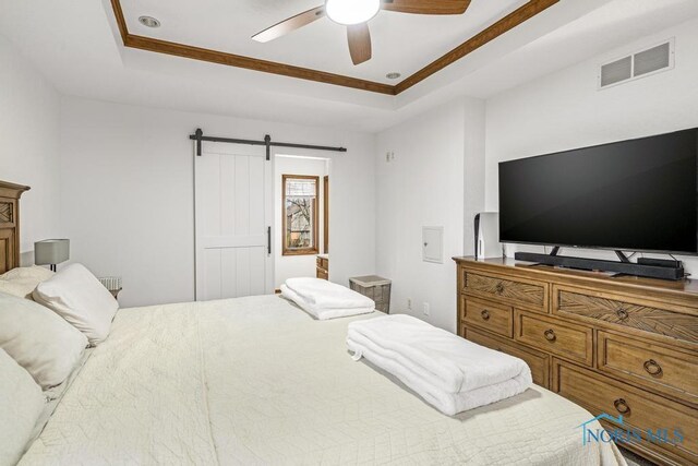 bedroom with a tray ceiling, a barn door, visible vents, and ceiling fan